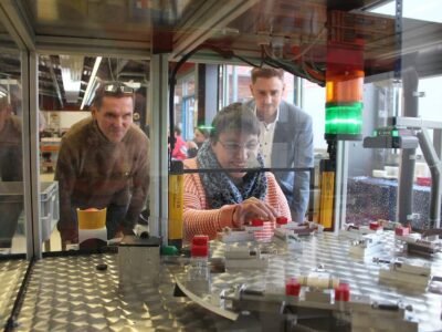 Auf die Bedürfnisse behinderter Menschen abgestimmte Modernisierung eines industriellen Arbeitsprozesses: Brigitte Lutz, Mitarbeiterin der Werkstatt Sennfeld, demonstriert Julius Kirchner (r.), geschäftsführender Gesellschafter FRÄNKISCHE Group, und Werkstattleiter Günter Scheuring den von FRÄNKISCHE-Azubis entwickelten Prüftisch für Fittings.