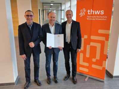 Dekan Prof. Dr. Johannes Paulus (li.) und der Präsident der THWS Prof. Dr. Dr. h. c. Robert Grebner (re.) überreichen Dr. Matthias Diemer die Urkunde zur Ernennung als Honorarprofessor (Foto: THWS/Martin Kraus)