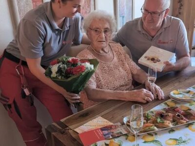 Michael Lindemann, Sachbearbeiter und Miriam Künzl, Einsatzdienstfahrerin im Hausnotruf in Schweinfurt überraschen Melina Bühner an ihrem 100. Geburtstag mit Blumen und Pralinen. Bildnachweis: Katharina Dietz